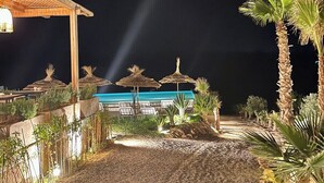 A nighttime view of a resort with a beach area, palm trees, and a building with a blue facade. - Laho Lodge (Lalla Takarkoust)