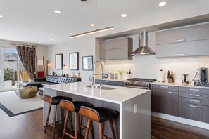 A modern kitchen with a large island, bar stools, and a dining area with a sofa. - Luxury 4BR | Near Swedish | Sauna + Hot Tub (Englewood)