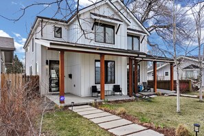 A two-story house with a covered porch and a small garden area. - Luxury 4BR | Near Swedish | Sauna + Hot Tub (Englewood)