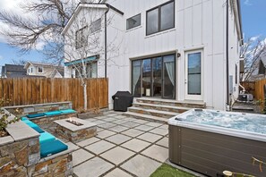 A backyard with a stone patio, a hot tub, and a wooden fence. - Luxury 4BR | Near Swedish | Sauna + Hot Tub (Englewood)