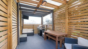 A covered outdoor patio with a grill, seating, and a TV.