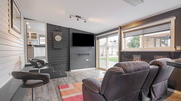 A modern living room with a sofa, a bar stool, and a TV. There is a large window with a view of the outdoors.