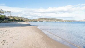 A beach with clear skies, calm water, and a distant town.