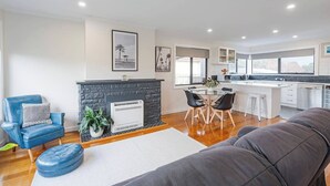 A modern living room with a fireplace, a dining area, and a kitchen with a large window.