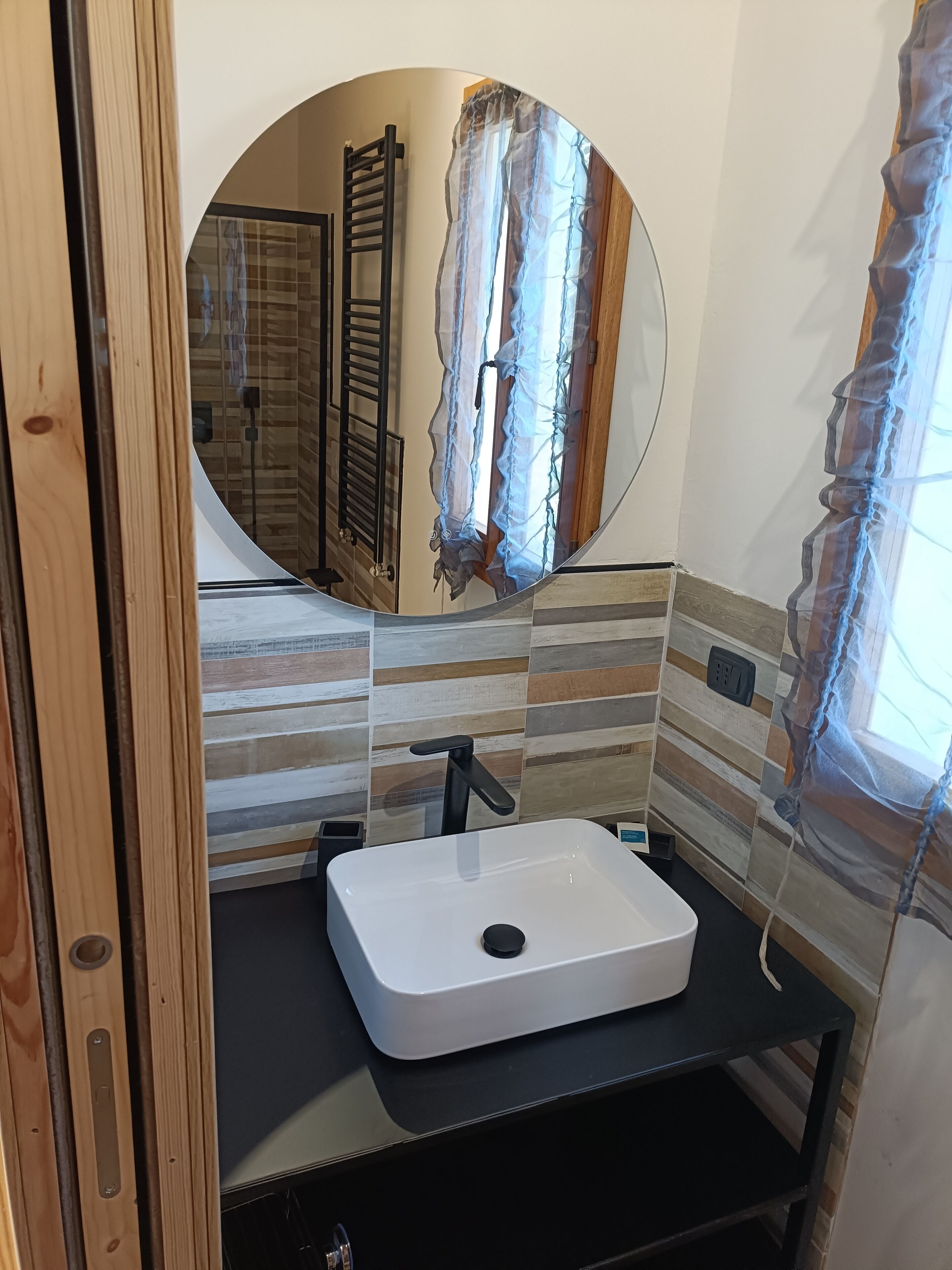 Un baño con un lavamanos blanco, un espejo redondo y una puerta de madera.