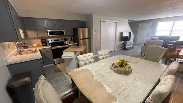 A modern kitchen with grey cabinets, stainless steel appliances, and a dining area with a large table and cushioned chairs.