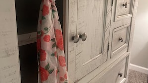A white wooden cabinet with three drawers and two doors, one of which has a floral curtain.