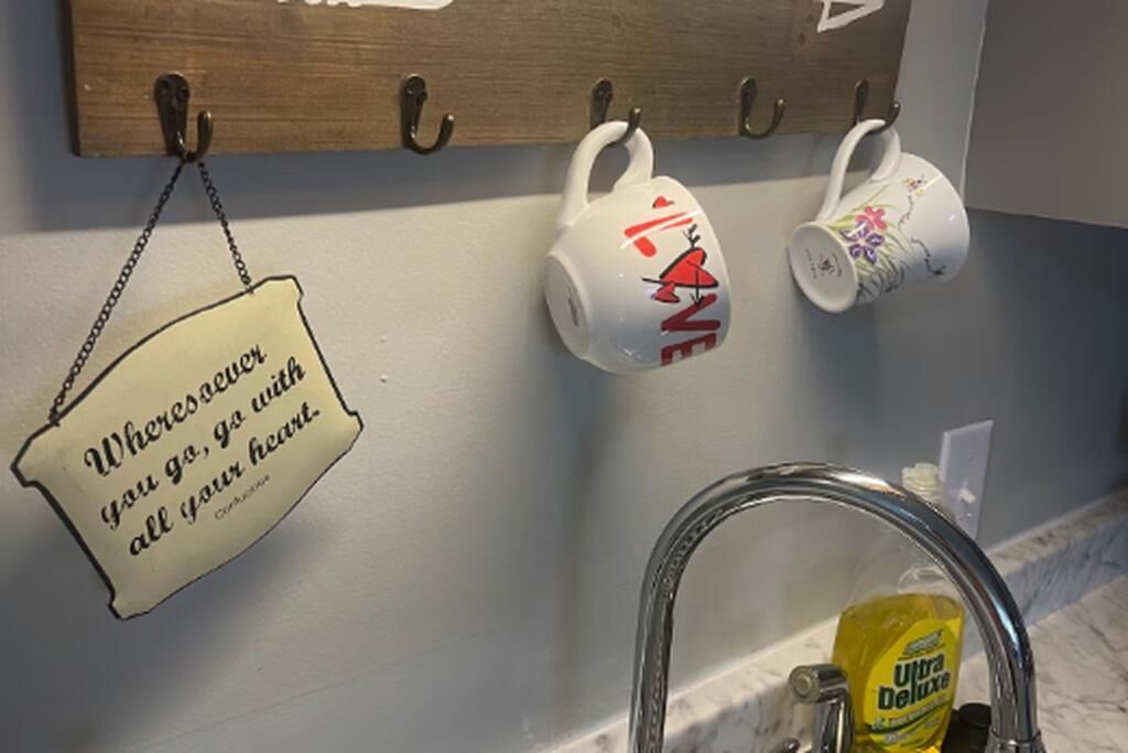 Een keuken met een houten rek voor kruiden, twee witte mokken met rode decoraties, en een roestvrijstalen kraan.