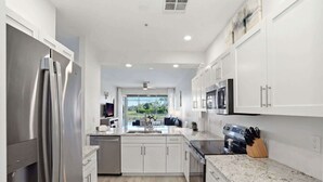 Una cocina moderna con electrodomésticos de acero inoxidable, armarios blancos y encimera de mármol.