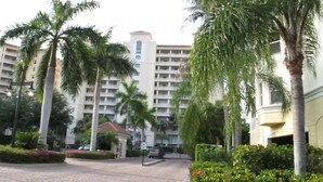 A multi-story hotel with a central courtyard, palm trees, and a red-roofed building. - Regatta at Vanderbilt Beach | Pool | Walk to Gulf (Naples)