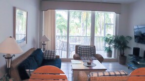 A living room with a sofa, armchairs, a coffee table, and a TV. There is a balcony with chairs and a table outside. - Regatta at Vanderbilt Beach | Pool | Walk to Gulf (Naples)