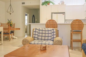 A cozy living room with a wooden coffee table, two wicker armchairs, and a dining area with a wooden table and chairs. - Regatta at Vanderbilt Beach | Pool | Walk to Gulf (Naples)