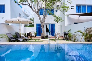 Zona de piscina con sillas de descanso, una mesa y una sombrilla.