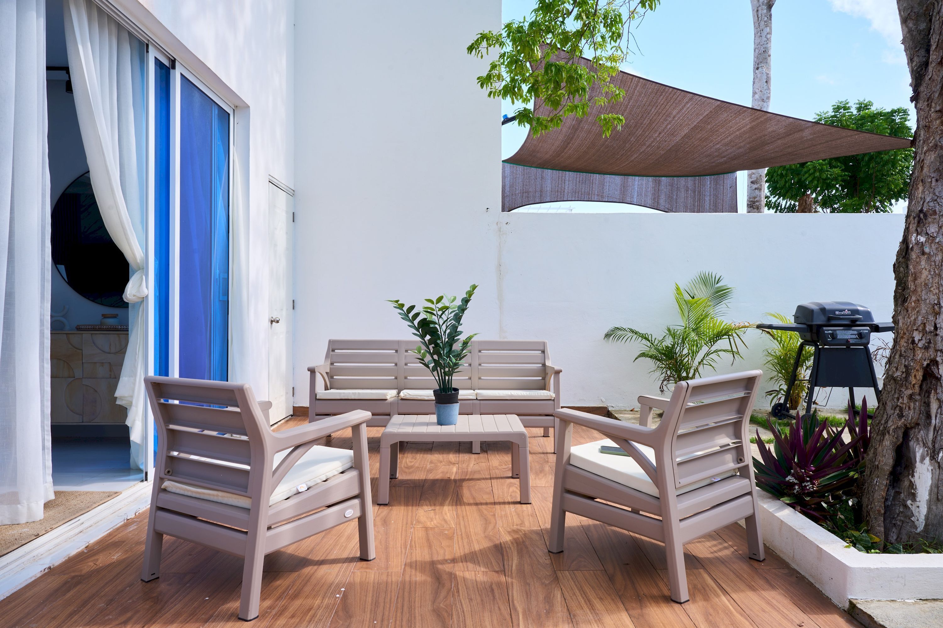Eine Terrasse mit einem Holztisch, vier Stühlen, einem Blumentopf und einem Grill.