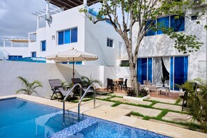 Un área de piscina moderna al aire libre, con piscina cristalina, sillones de descanso y una mesa de comedor con sillas.