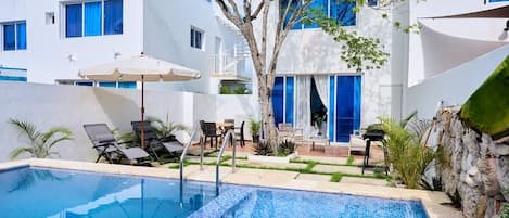 A swimming pool with tiled blue edges, surrounded by lounge chairs and a small table.