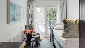 A modern bedroom with a bed, a chair with a vase of flowers, and a view of the outdoors. - Hambo Hideaway - Private guest house with fenced patio near Malmö & Lund (Staffanstorp)
