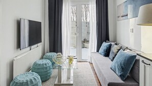 A modern living room with a glass coffee table, grey sofa with blue cushions, and a flat-screen TV mounted on the wall. - Hambo Hideaway - Private guest house with fenced patio near Malmö & Lund (Staffanstorp)