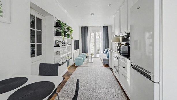 A modern kitchen with white cabinets, a built-in oven, and a large refrigerator. There is a dining area with a table and chairs, and a seating area with a sofa and ottomans. - Hambo Hideaway - Private guest house with fenced patio near Malmö & Lund (Staffanstorp)
