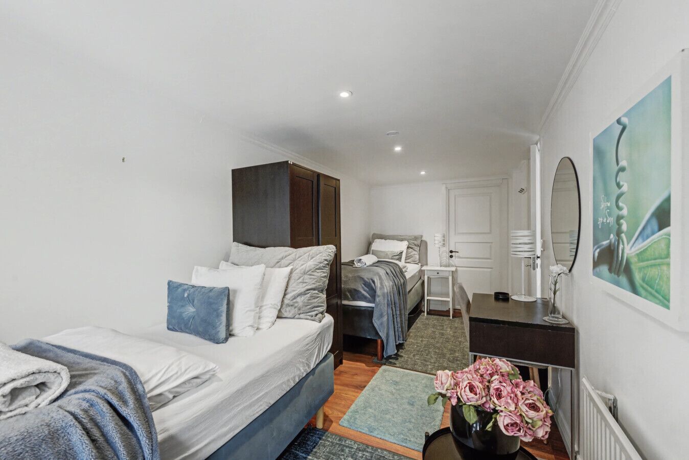 Una habitación compacta con una cama, un escritorio y una silla. Hay un espejo en la pared, una puerta y un radiador.