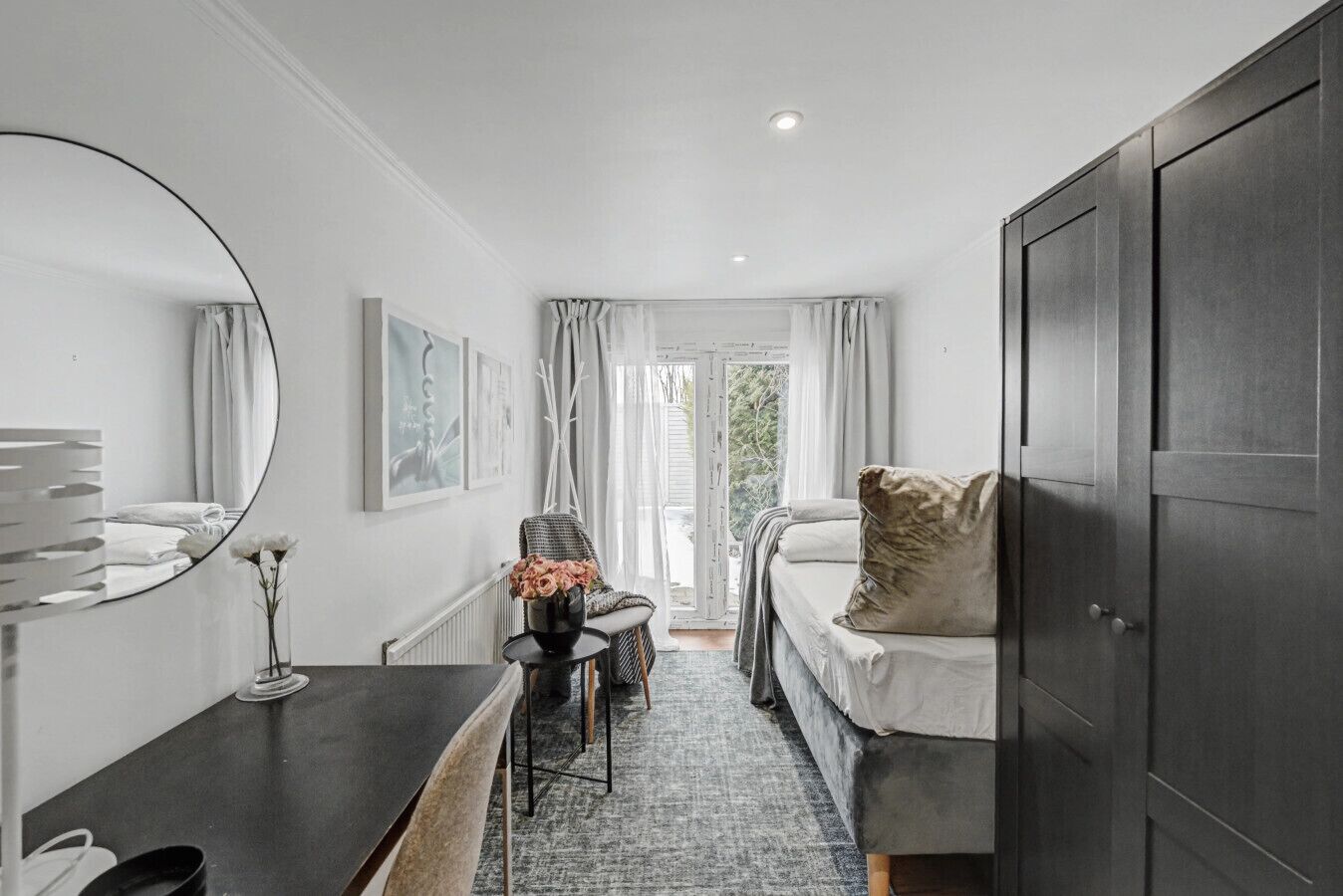 A modern bedroom with a bed, a desk, a chair, a mirror, and a wardrobe.