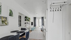 A modern kitchen with white cabinetry, a dining area with a table and chairs, and a hallway leading to a bedroom. - Hambo Hideaway - Private guest house with fenced patio near Malmö & Lund (Staffanstorp)