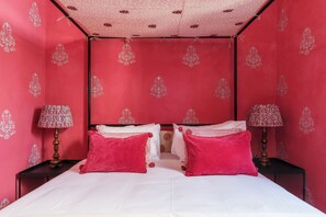 Una habitación con paredes rosas, una cama con ropa de cama blanca y dos mesitas de noche con lámparas.