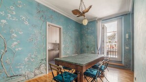 En matplats med ett träbord och blå, vadderade stolar, en väggmålning med blommotiv och en hängande lampa.