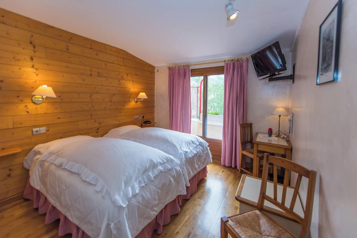 Ein Zimmer mit zwei Betten, einem Schreibtisch mit Stuhl, einem Fernseher und einem Fenster mit Vorhängen.