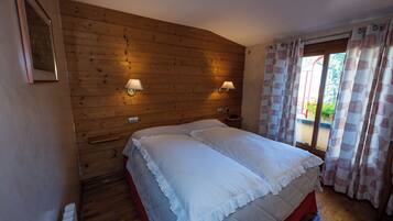 A bedroom with a wooden headboard, two bedside lamps, a bed with white bedding, and a window with patterned curtains.