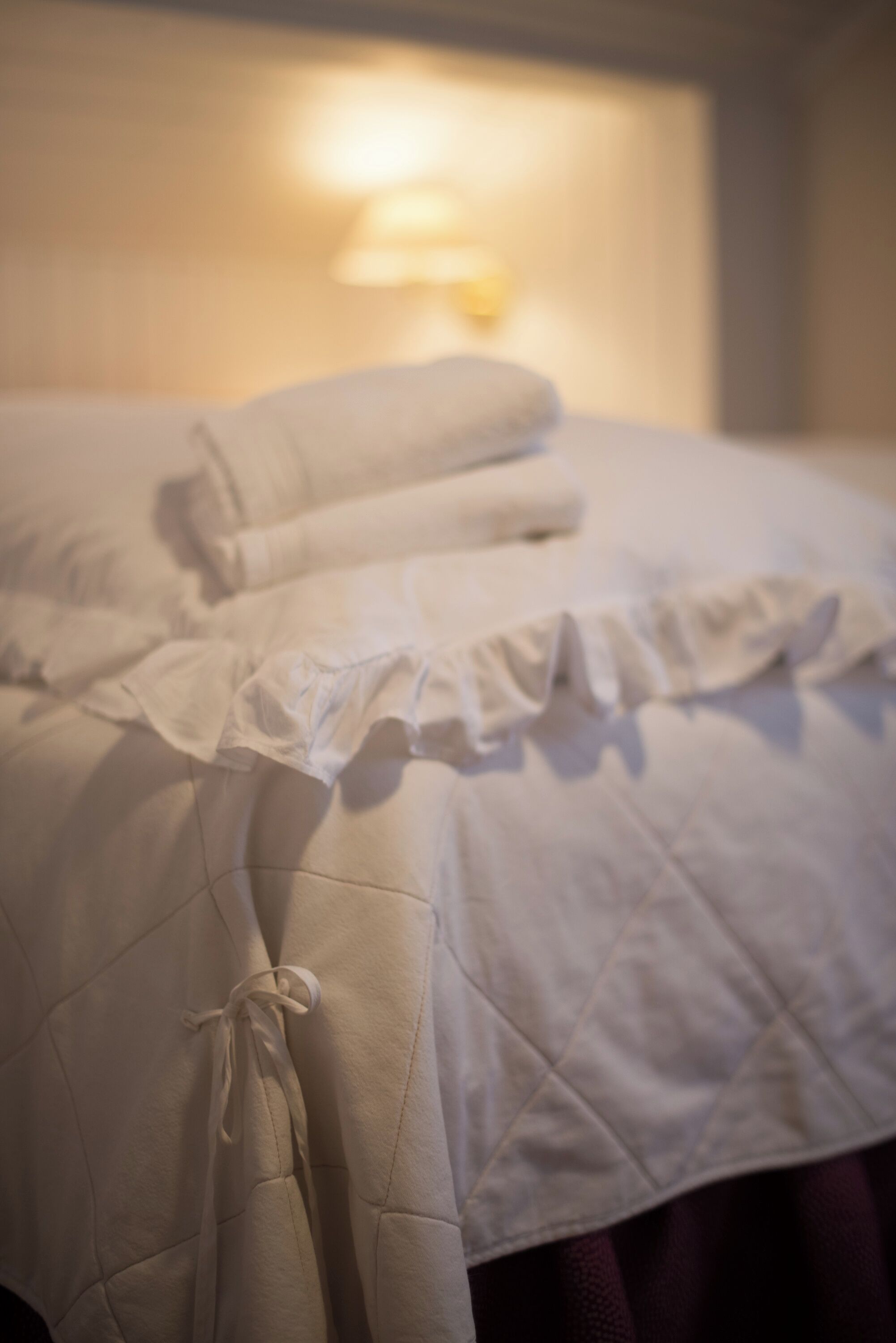 A bed with a quilted cover and pillows, a wall-mounted light, and a visible window.