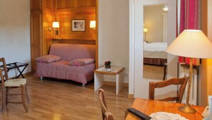 Una habitación con panel de madera, una cama, una mesita de noche con lámpara, una silla y un escritorio con control remoto.