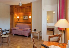 Um quarto com painel de parede de madeira, uma cama, uma mesinha com abajur, uma cadeira e uma escrivaninha com controle remoto.