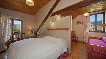 Un dormitorio con una cama grande, una cama más pequeña, vigas de madera, una ventana y una silla.