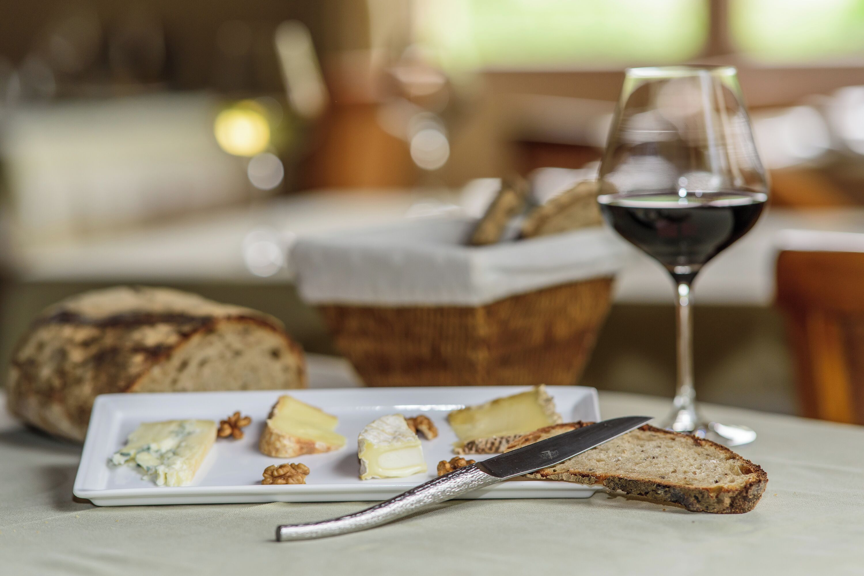 Un plato con queso, nueces, pan, un cuchillo y una copa de vino tinto sobre una mesa.