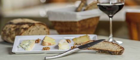 Un plato con queso, nueces, pan, un cuchillo y una copa de vino tinto sobre una mesa.