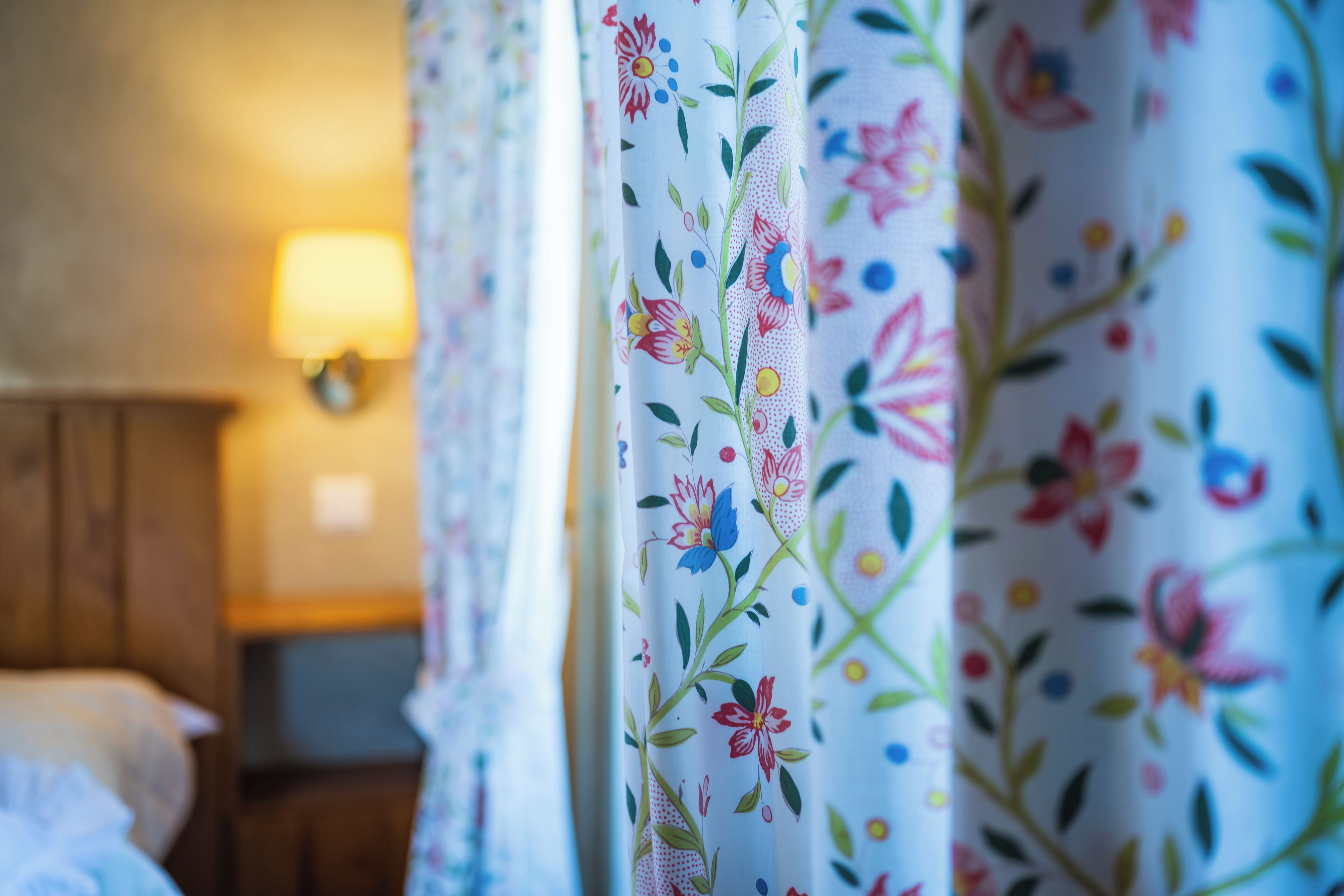A hotel room with floral curtains, a bed, and a bedside lamp.