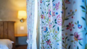 A hotel room with floral curtains, a bed, and a bedside lamp.