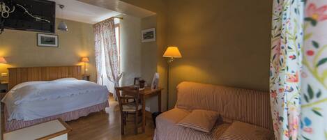 A room with a bed, a desk, a chair, a sofa, and a lamp.