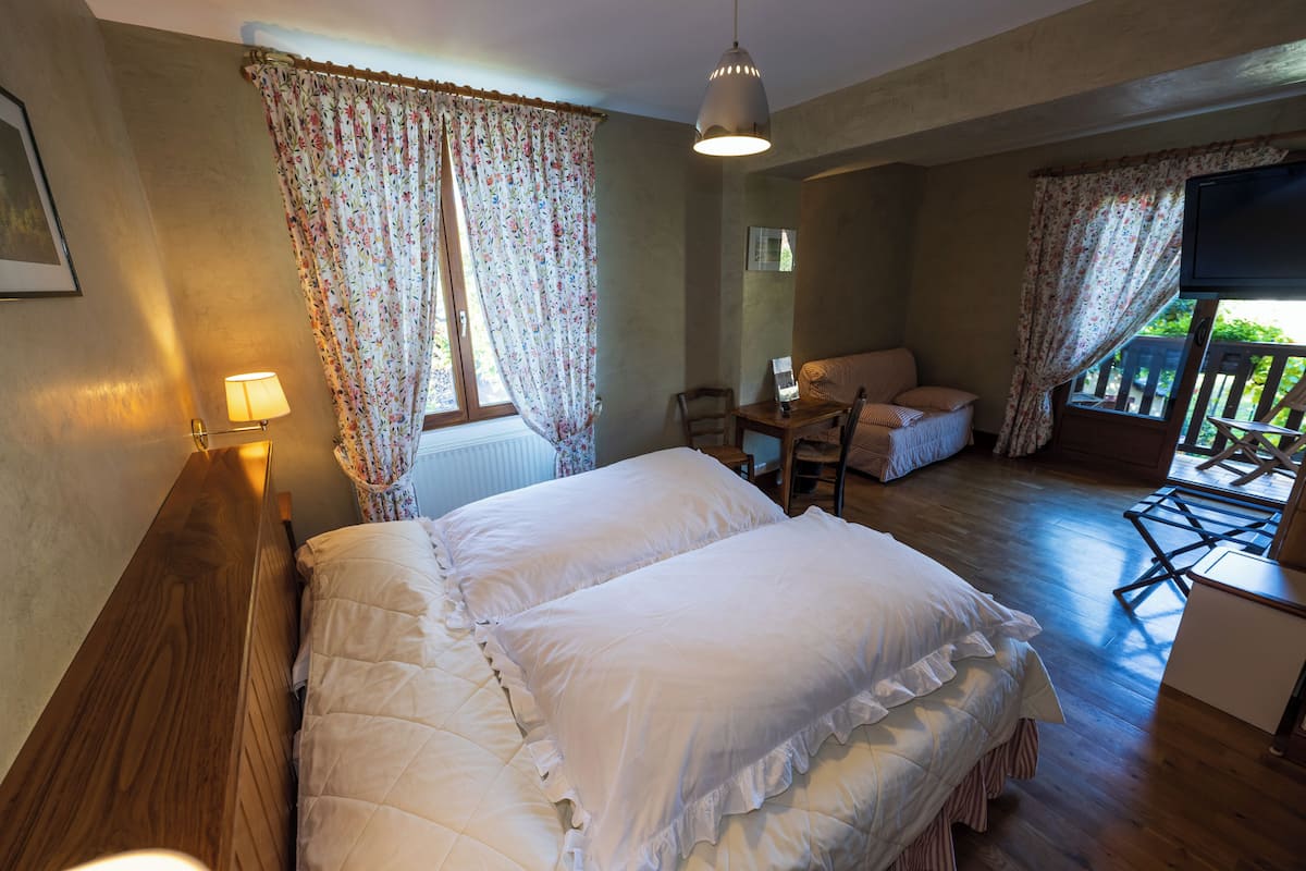 Ein Schlafzimmer mit Bett, Schreibtisch und Stuhl, einem Fenster mit Vorhängen sowie einem an der Wand montierten Fernseher.