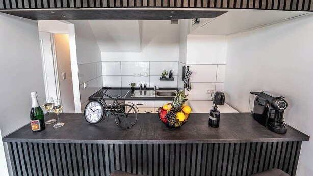 A modern kitchen with a dark countertop, a bicycle, a fruit bowl, and a coffee machine. - Stern Blick: Maisonette, Balkon, zentral in Bremen (Bremen)