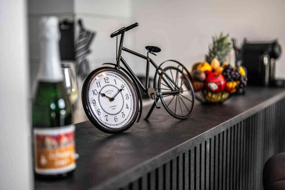 A kitchen counter with a vintage bicycle, a clock, and a fruit bowl.