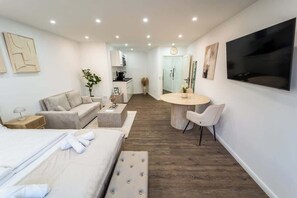 Habitació d'hotel moderna amb un llit, un sofà, zona de menjador amb taula i cadires, televisió i obres d'art a les parets.