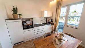 A modern kitchen with white cabinets, a wooden dining table, and a view of the city through large windows. - Stadionperle | Direkt im Viertel | Gruppenliebling (Bremen)