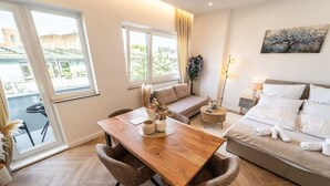 A modern hotel room with a wooden dining table, a sofa, a bed, and a large window offering a view of the outside. - Stadionperle | Direkt im Viertel | Gruppenliebling (Bremen)
