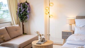 A modern hotel room with a sofa, a round side table with a vase and remote, a bed with pillows, a nightstand with a lamp, and a wall-mounted light fixture. - Stadionperle | Direkt im Viertel | Gruppenliebling (Bremen)