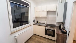 Een compacte keuken met witte kasten, een inbouwoven en een raam met uitzicht op een woonwijk.