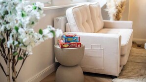 Un salon chaleureux avec un canapé beige, une petite table ronde sur laquelle se trouve une boîte de céréales et un vase rempli de fleurs blanches.