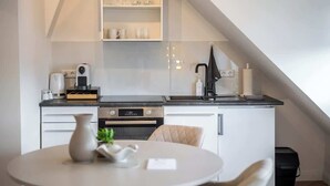 Une cuisine moderne avec des meubles blancs, un four encastré, une machine à café et un coin repas comprenant une table et des chaises.
