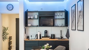 Cocina compacta con microondas, cafetera y lavabo. Zona de comedor con mesa y sillas.